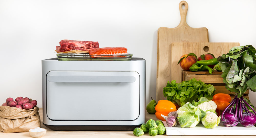 The Brava Oven on a kitchen countertop surrounded by fresh produce and meats
